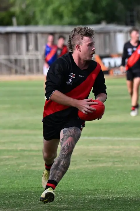 A Waaia footballer in the red and black running with the ball