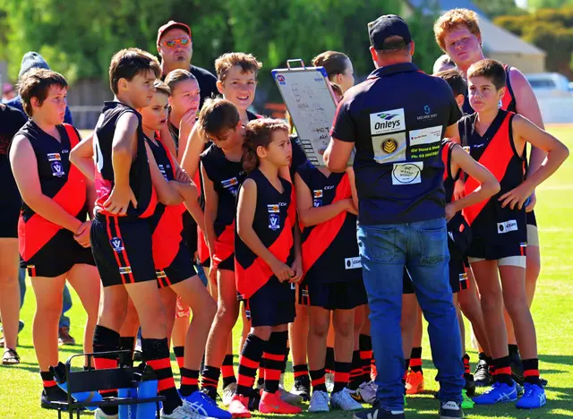 Waaia junior footballers in red and black gathered with their coach